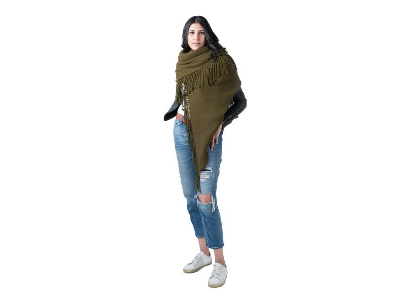 Woman wearing a handwoven alpaca scarf in moss green, styled diagonally across the body with fringe detail, paired with distressed jeans and sneakers.