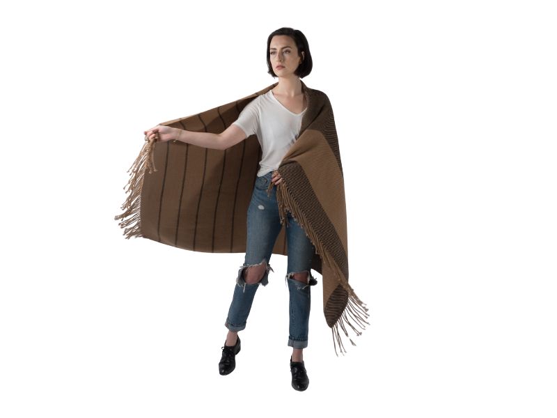 Woman holding open a large striped alpaca scarf to reveal its full size, styled with a white tee and distressed jeans against a neutral backdrop.
